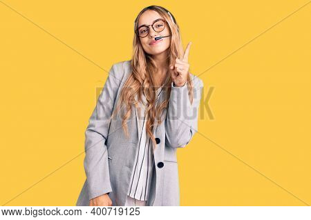 Young beautiful blonde woman wearing call center agent headset showing and pointing up with finger number one while smiling confident and happy. 