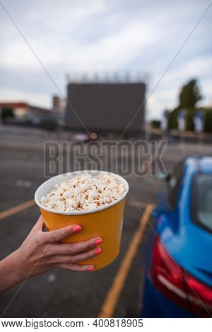 Seletive Focus On Woman Hand Holding Big Yellow Popcorn Bucket At Autocinema During Evening Movie Se