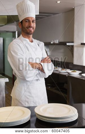 Happy head chef standing with arms crossed behind counter in a commercial kitchen