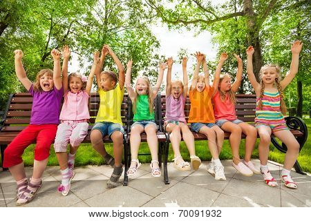 Funny group of kids on bench with arms up