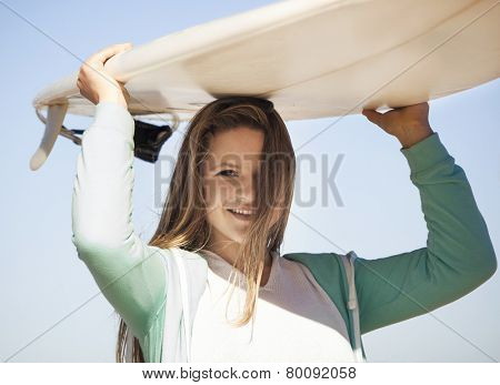 Tenage girl in the beach and holding a surfboard over her head