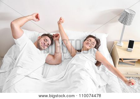 Happy couple waking up with mobile alarm clock