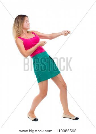 back view of standing girl pulling a rope from the top or cling to something. girl  watching.  Isolated over white background. The blonde in a green skirt and pink blouse pulling a rope over.
