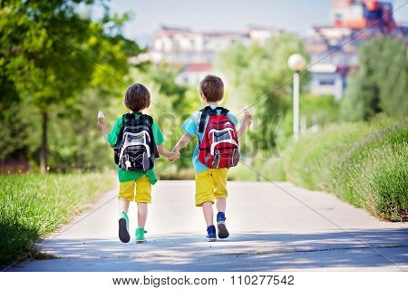 Two Adorable Boys In Colorful Clothes And Backpacks, Walking Away, Holding And Eating Ice Cream