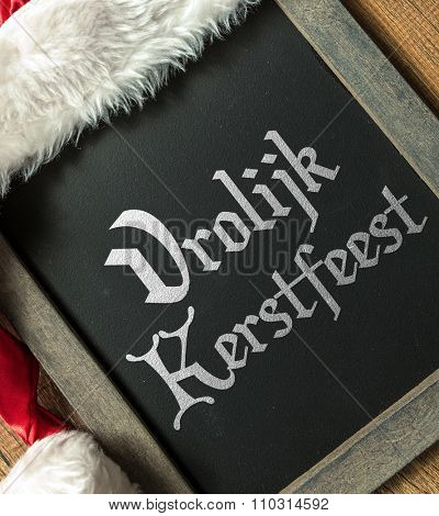 Merry Christmas (in Dutch) written on blackboard with santa hat
