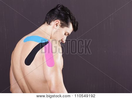 Muscular man with kinesiotaping on the shoulder against grunge background