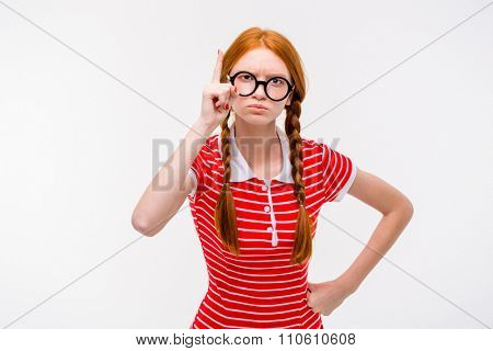 Strict young redhead woman with two braids in round glasses pointing up isolated on white background