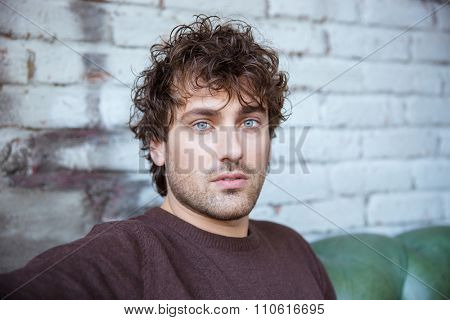 Closeup of attractive thoughtful sad curly male against a brickwall
