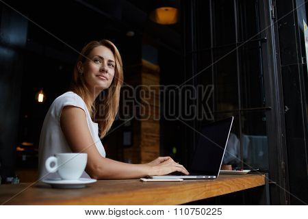 Young charming female freelancer thinking about new ideas during work on laptop computer