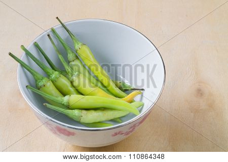 Green pepper in a cup of white wooden background.