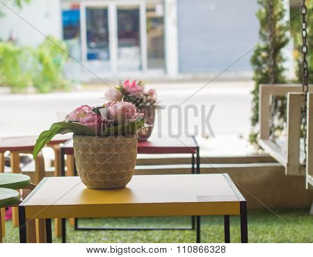 Place the vase on a wooden table outside the coffee shop.
