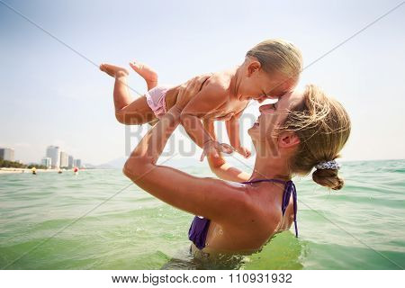Closeup Side-view Mother Holds Small Daughter Both Smile In Sea