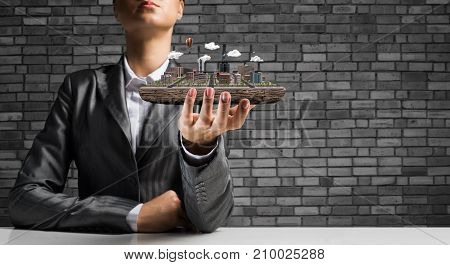 Cropped image of businessman in suit presenting in his hand modern city block with gray brick wall on background. 3D rendering.