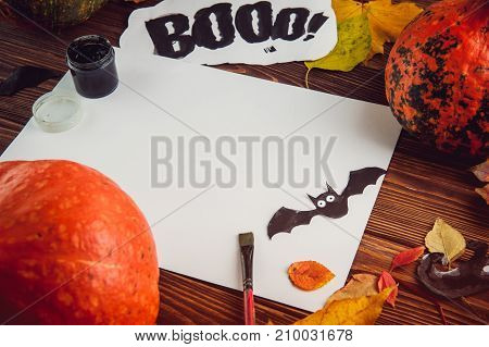 Halloween holiday background. Prepearing for party. Fresh pumpkins, coloured leaves, art, craft and painting materials on dark wooden table. Selective focus, top view. Space for text.