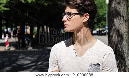 Stylish Young Handsome Man Standing in City Park, Looking to a Side
