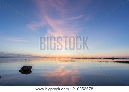 Evening sunlight on coast pink clouds blue sky reflection on water. Beach in summer. Seaside natural environment. Shore in Kesselaid small island in Estonia. Nature Reserve in North Europe