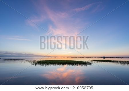 Evening sunlight on coast pink clouds blue sky reflection on water. Beach in summer. Seaside natural environment. Shore in Kesselaid small island in Estonia. Nature Reserve in North Europe