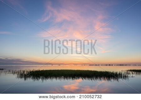 Evening sunlight on coast pink clouds blue sky reflection on water. Beach in summer. Seaside natural environment. Shore in Kesselaid small island in Estonia. Nature Reserve in North Europe