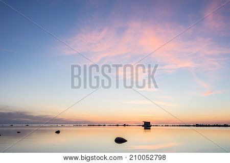 Evening sunlight on coast pink clouds blue sky reflection on water. Beach in summer. Seaside natural environment. Shore in Kesselaid small island in Estonia. Nature Reserve in North Europe