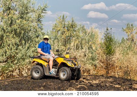 Caucasian man in sport protective goggles riding an ATV quad bike over rough terrain with meadows of dry autumn grass. Adventure activity concept.
