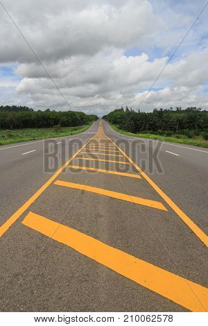 Long hilly road passes through green countryside with cloundy sky.