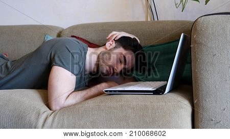 Close Up of Tired Young Man with Dark Hair Falling Asleep while Working Laptop Computer on a Couch