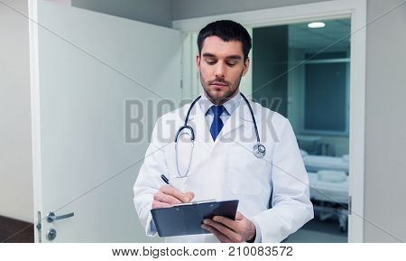medicine, healthcare and people concept - doctor writing to clipboard at hospital