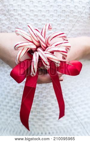 Woman holding Merry Christmas Candy Canes and a red bow in a white sweater in front of a rustic background with room for copy