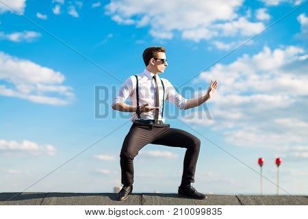 Young Serious Busunessman In White Shirt, Tie, Braces And Sunglasses Trains On The Roof