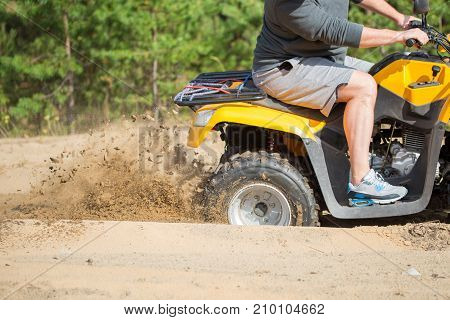An Atv Quadbike Get Stuck In A Sandy Road Near Forest And Having Wheel-spin Making A Spray Of Sand.