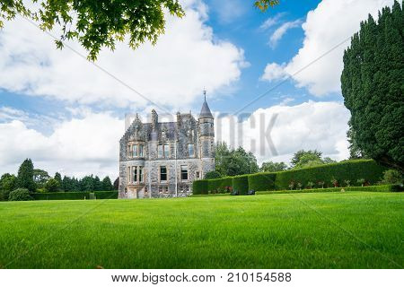 Large green lawn and gardens in front of distant stone castle under blue sky with large white clouds.
