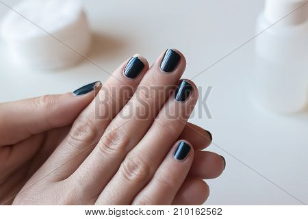 Shabby dark blue manicure. Threadbare nail polish. Woman hands on white table