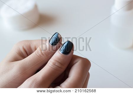 Old dark blue manicure. Shabby nail polish. Woman hands on white table. Spa.