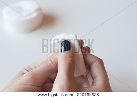 Woman removes the nail polish. Hands with dark blue manicure on whote table.