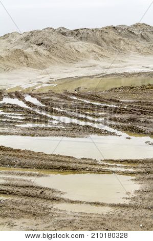wet scenery with skidmarks around a light brown heap of earth