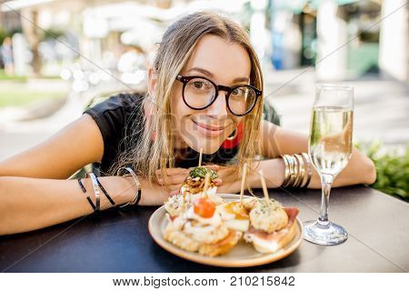 Young woman enjoying tasty appetizer with pinchos, traditional spanish snack, and glass of wine sitting outdoors at the bar in Valencia city