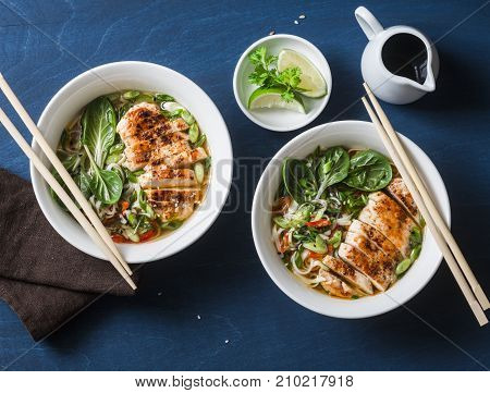 Asian style spicy udon noodle soup with fried chicken on a blue background top view