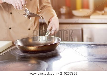 Chef pouring oil in frying pan. Male chef in gloves going to fry duck breast. Cook preparing meat.