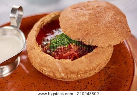 Delicious red soup with parsley. Ukrainian and russian national borshch in bread pot. Tasty beetroot soup with beef meat and sour cream.