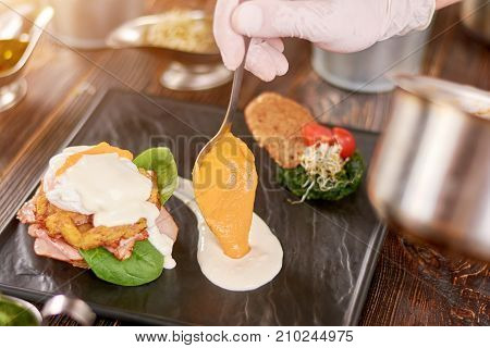Cooking delicious benedict in restaurant. Chef hand serving tasty benedict with sauce. Food preparing and culinary.