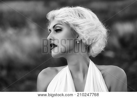 Closeup portrait of one attractive sensual dreaming young retro woman with blonde hair red lips in white dress in monroe style outdoor on natural background horizontal picture