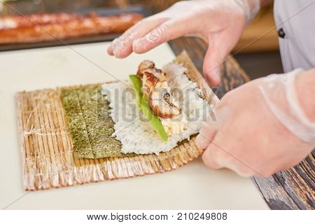 Cook hands making japanese sushi roll. The process of cooking sushi roll with eel, avocado, rice and nori. Preparing of roll unagi furay.