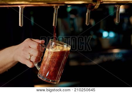 Pouring fresh alcoholic beverage. Batender hand pouring fresh ale beer in glass from beer tap in pub or restaurant.