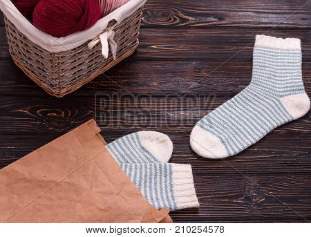 Knitted socks and basket with yarn on wooden background. White striped socks