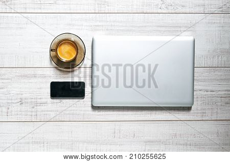 View of a wooden table with a laptop, a mobilephone and a cup of coffee on it