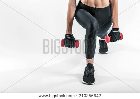 Low section of a sportswoman holding pink dumbbells wears black leggins o nwhite isolated background