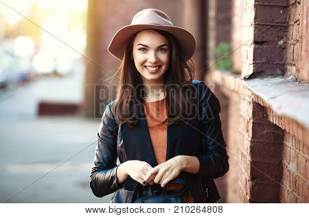 Close-up Fashion woman portrait of young pretty trendy girl posing at the city, autumn street fashion, holding retro fedora hat popular until the 60s. laughing and smiling portrait.trendy