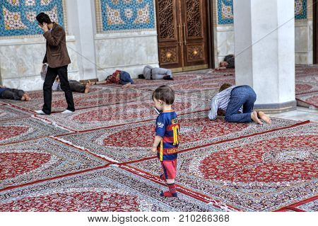 Fars Province Shiraz Iran - 19 april 2017: Shah Cheragh Shrine A little boy is talking on a mobile phone in the inner courtyard of the mosque near Muslims are praying and sleeping.