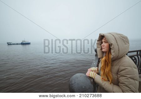 Woman standing alone at sea coast and looking on ship. Winter time. Seaman's wife.