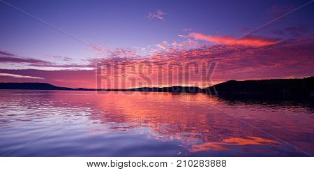 Vivid pink magenta glowing sunrise over water with clear water reflections. Lake Macquarie Australia.